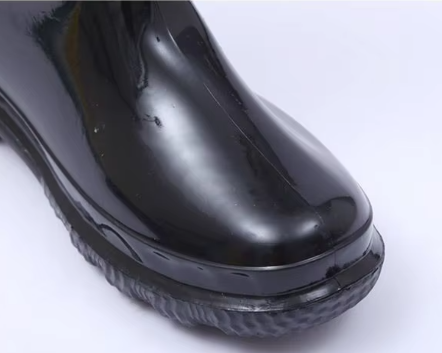 a092bfdc-7822-4703-8756-0930a4d9c5b3_Nahaufnahme der abgerundeten Zehenkappe an einem glänzend schwarzen, warmen, PVC‑wasserdichten Arbeitsschuh.png
